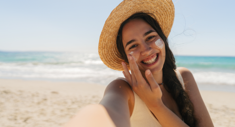 A woman in a straw hat relaxes on the beach, with the sea and sand visible around her.